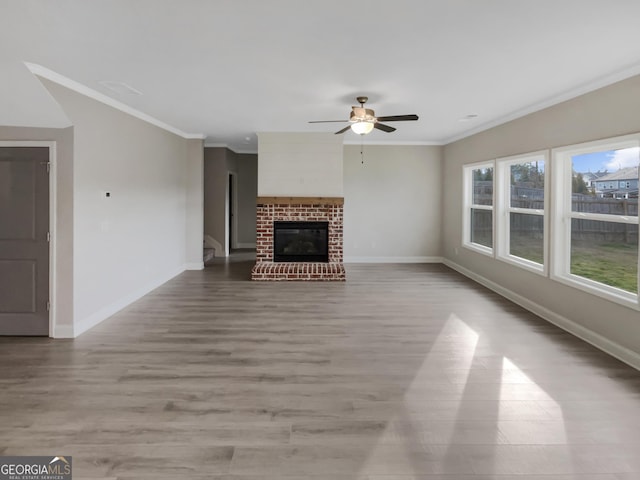 unfurnished living room with light wood-type flooring, a brick fireplace, baseboards, and crown molding