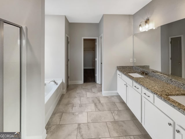 full bath with a walk in closet, a garden tub, double vanity, a sink, and baseboards