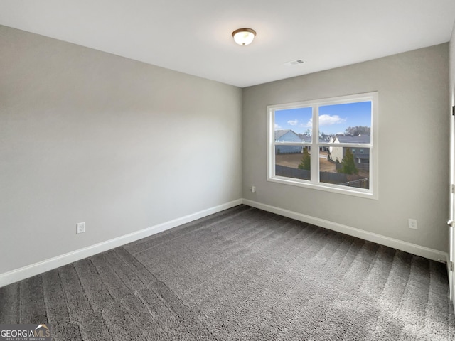 spare room with dark colored carpet, visible vents, and baseboards