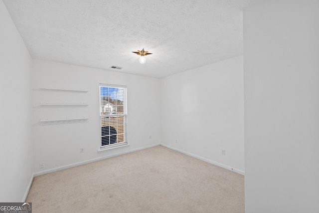 empty room featuring a textured ceiling, carpet, visible vents, and baseboards