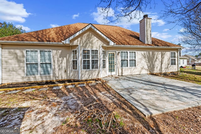 rear view of house with a shingled roof, a patio, and a chimney