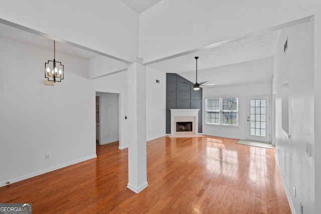 unfurnished living room with baseboards, a towering ceiling, light wood-style flooring, a fireplace, and ceiling fan with notable chandelier