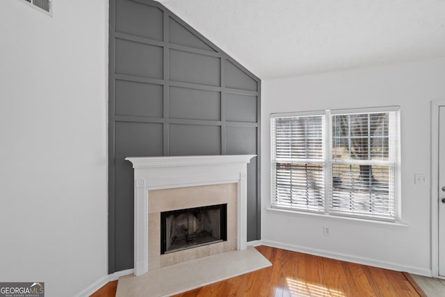 unfurnished living room featuring visible vents, a decorative wall, a high end fireplace, wood finished floors, and baseboards