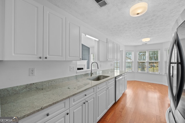 kitchen featuring visible vents, white cabinets, light wood-style flooring, stainless steel appliances, and a sink