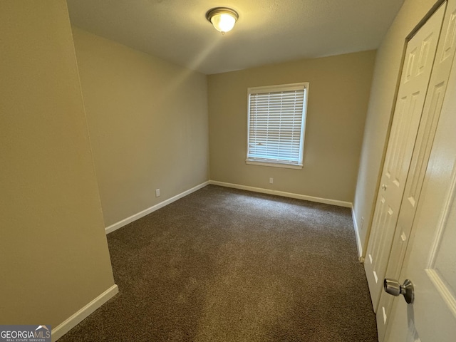 unfurnished bedroom with dark colored carpet and baseboards