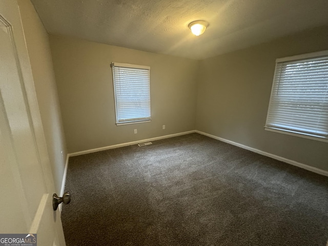 carpeted spare room with visible vents, a textured ceiling, and baseboards