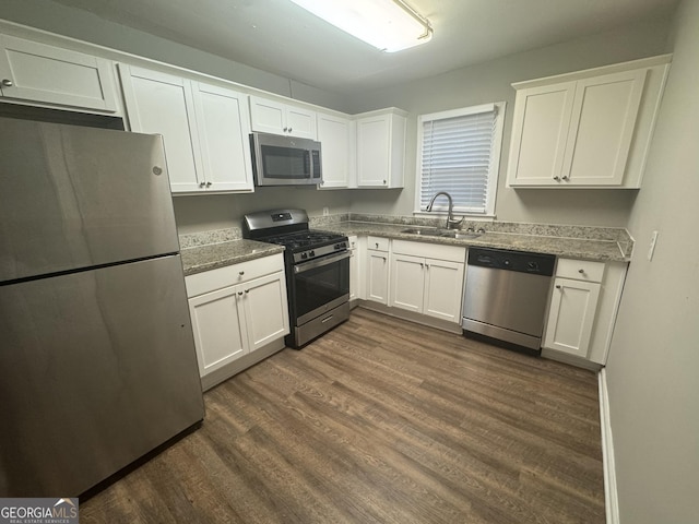 kitchen with dark wood-style floors, appliances with stainless steel finishes, white cabinetry, a sink, and light stone countertops