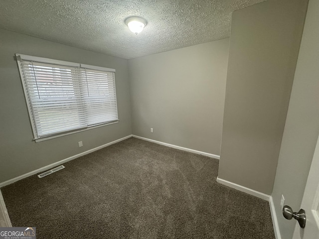 unfurnished room with a textured ceiling, dark colored carpet, visible vents, and baseboards