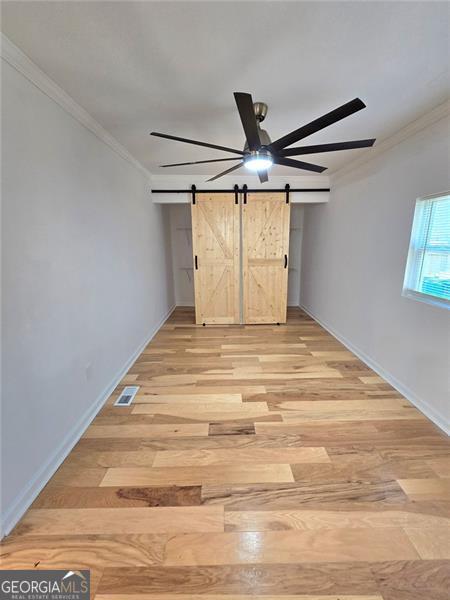 unfurnished bedroom featuring light wood finished floors, a barn door, visible vents, ceiling fan, and ornamental molding