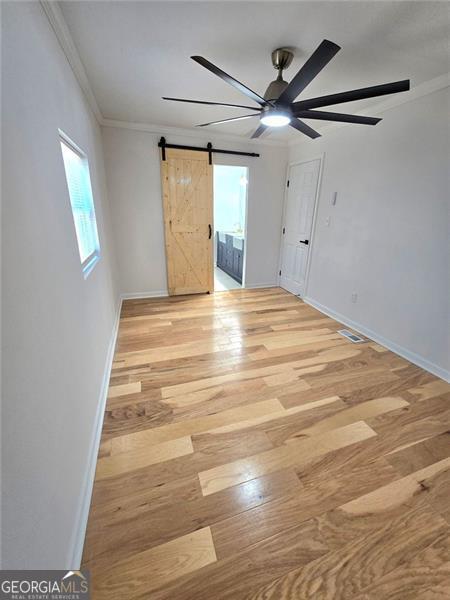 spare room featuring a barn door, visible vents, light wood-style flooring, and crown molding