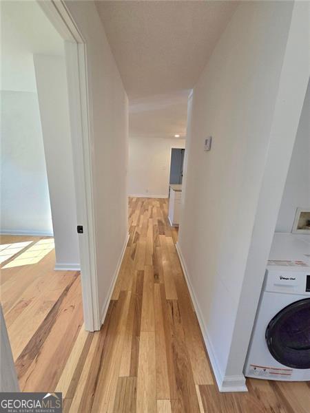 hall featuring washer / dryer, baseboards, and light wood-style floors