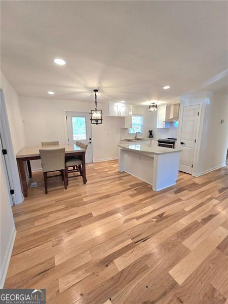 kitchen with recessed lighting, light countertops, light wood-style flooring, white cabinetry, and wall chimney range hood