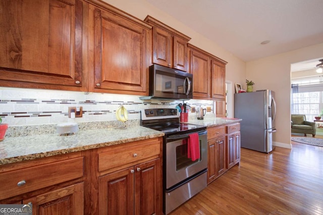 kitchen with light wood-style flooring, light stone countertops, appliances with stainless steel finishes, brown cabinets, and tasteful backsplash