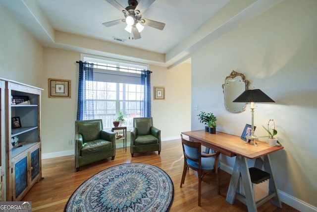 home office featuring baseboards, visible vents, a ceiling fan, wood finished floors, and a tray ceiling