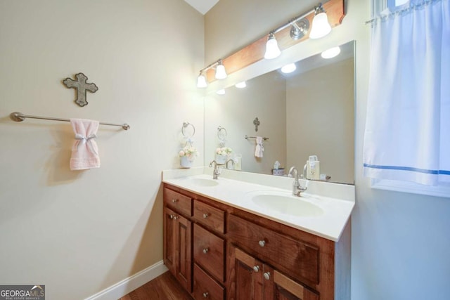 full bath with double vanity, wood finished floors, a sink, and baseboards