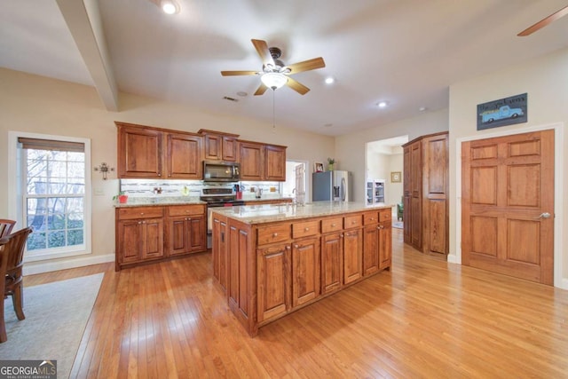 kitchen featuring stainless steel appliances, light wood finished floors, a kitchen island, and brown cabinets