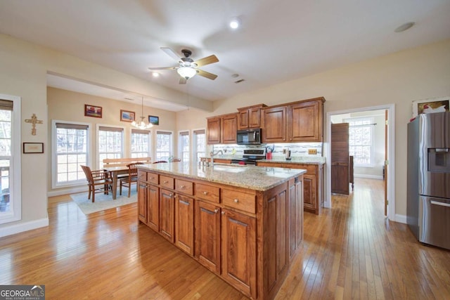 kitchen with a kitchen island, light wood-style floors, appliances with stainless steel finishes, brown cabinetry, and pendant lighting