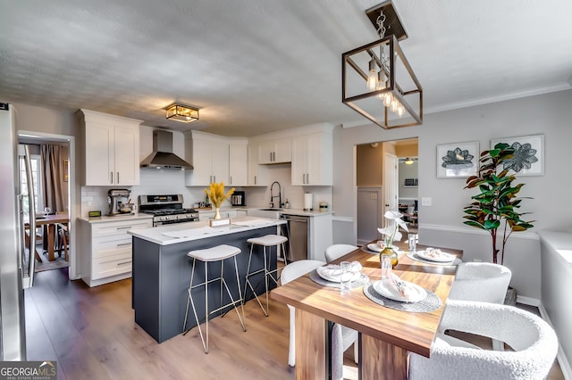 kitchen with a center island, stainless steel appliances, white cabinetry, a sink, and wall chimney range hood