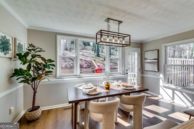 dining space featuring a textured ceiling, baseboards, wood finished floors, and crown molding