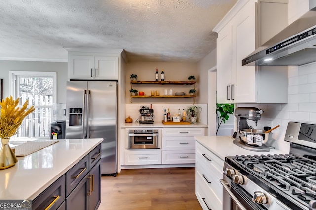 kitchen with white cabinets, appliances with stainless steel finishes, wood finished floors, light countertops, and wall chimney range hood