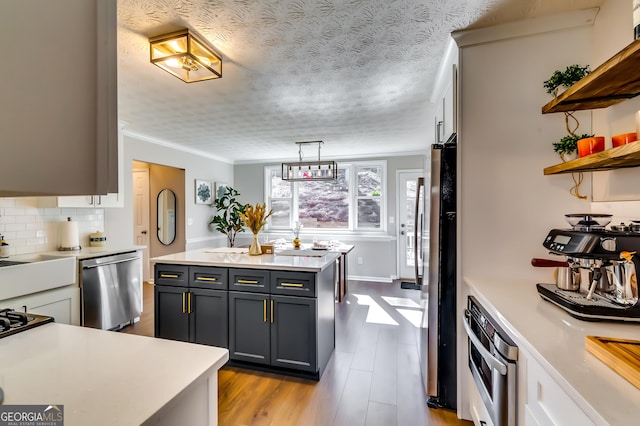 kitchen featuring pendant lighting, open shelves, stainless steel appliances, gray cabinets, and light countertops