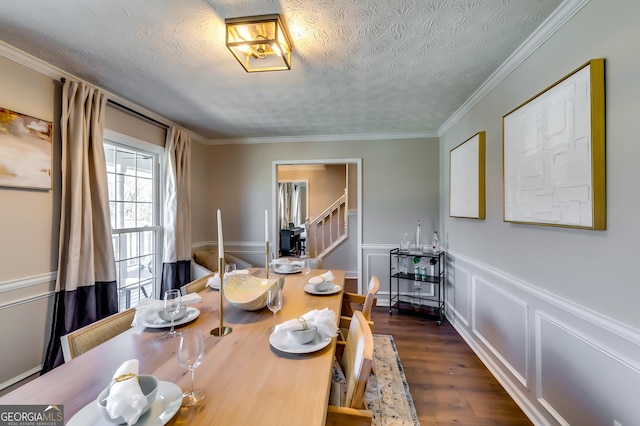 dining room featuring a textured ceiling, dark wood-type flooring, stairs, ornamental molding, and wainscoting