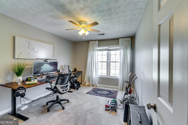 carpeted office space with a ceiling fan, visible vents, a textured ceiling, and baseboards