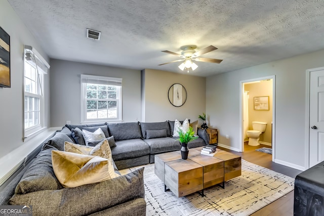 living room with a textured ceiling, light wood-type flooring, a ceiling fan, and baseboards