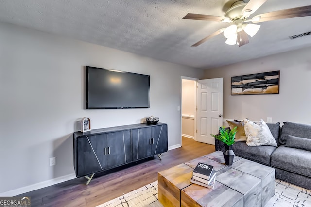 living area with ceiling fan, a textured ceiling, wood finished floors, visible vents, and baseboards