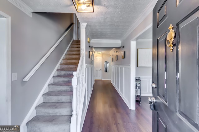 foyer entrance with a textured ceiling, stairs, wainscoting, dark wood finished floors, and crown molding