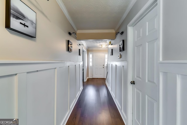 hallway featuring dark wood finished floors, wainscoting, ornamental molding, a textured ceiling, and a decorative wall