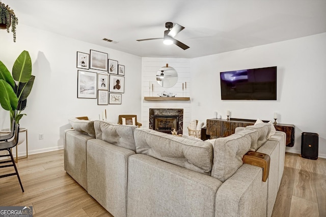 living area with ceiling fan, a fireplace, visible vents, baseboards, and light wood finished floors