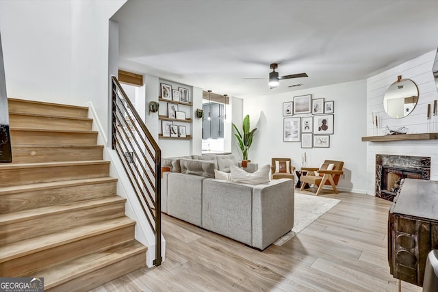 living area with a fireplace, visible vents, stairway, ceiling fan, and light wood-type flooring