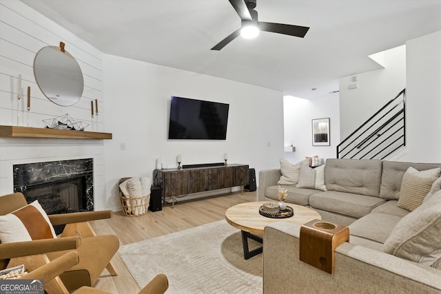 living area with light wood-type flooring, stairs, a premium fireplace, and a ceiling fan