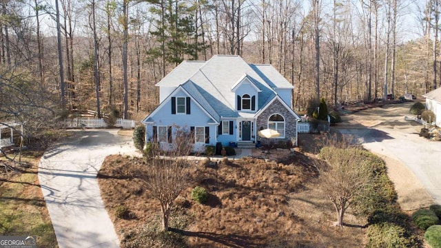 view of front of home featuring stone siding, fence, a view of trees, and concrete driveway