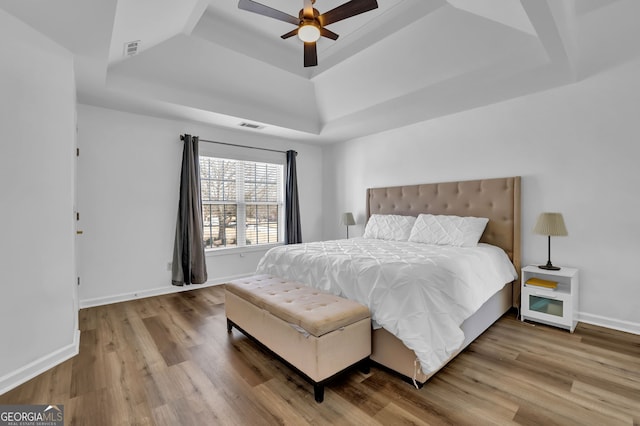 bedroom with a tray ceiling, visible vents, baseboards, and wood finished floors