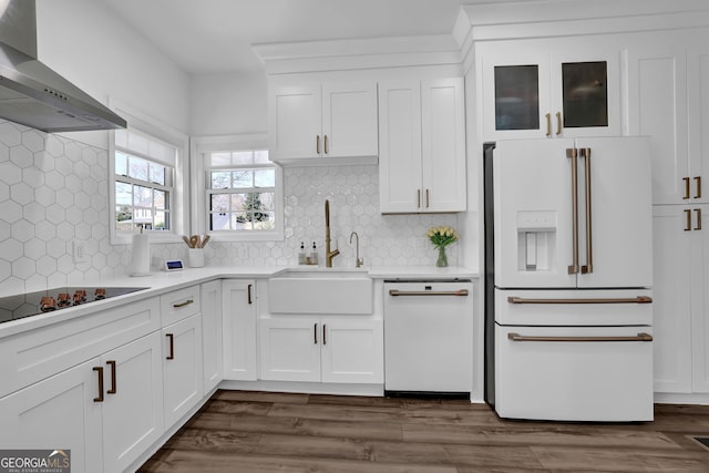 kitchen with white appliances, a sink, white cabinets, wall chimney range hood, and dark wood finished floors