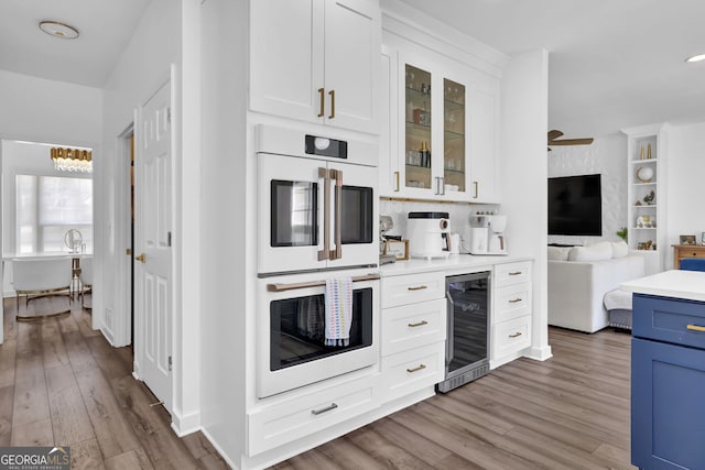 kitchen featuring beverage cooler, white cabinets, white double oven, glass insert cabinets, and wood finished floors