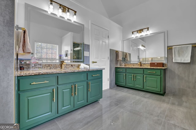 full bathroom featuring vaulted ceiling, a sink, two vanities, and tile walls