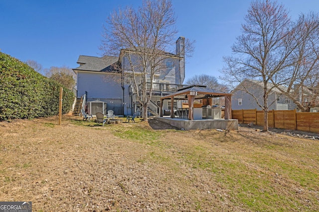 rear view of property with a fenced backyard, a chimney, stairs, a gazebo, and a patio area