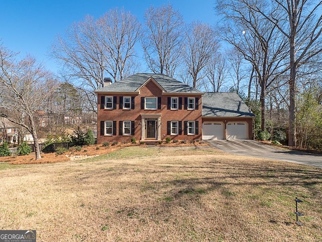 colonial house with a garage, brick siding, driveway, a chimney, and a front yard