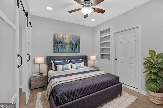 bedroom featuring a barn door, baseboards, light wood-style flooring, and recessed lighting