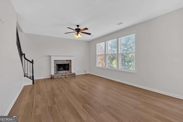 unfurnished living room with baseboards, visible vents, stairway, a stone fireplace, and light wood-style floors