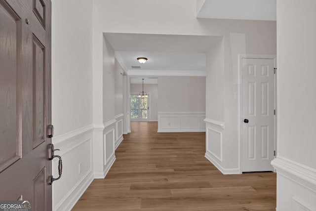 corridor with light wood-style flooring, crown molding, a notable chandelier, and a decorative wall