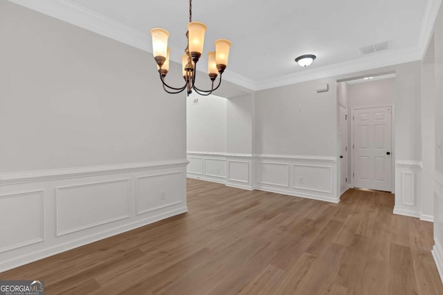 unfurnished dining area with visible vents, a decorative wall, ornamental molding, wood finished floors, and a chandelier