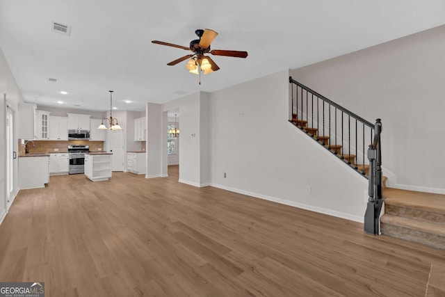 unfurnished living room with stairs, light wood finished floors, visible vents, baseboards, and ceiling fan with notable chandelier