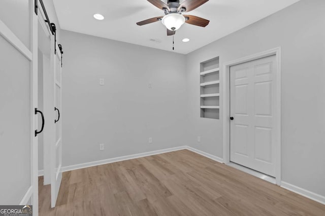 unfurnished bedroom featuring light wood finished floors, baseboards, and a barn door