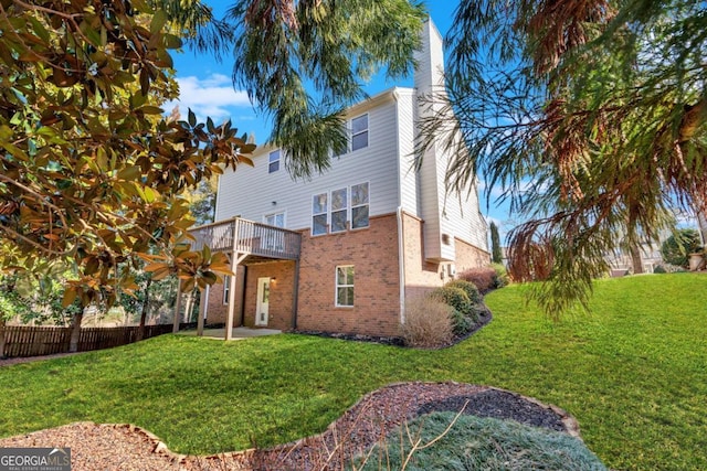 rear view of property with brick siding, a yard, a chimney, and fence