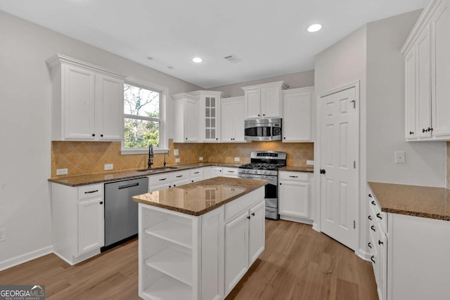 kitchen with stainless steel appliances, white cabinetry, a center island, open shelves, and glass insert cabinets