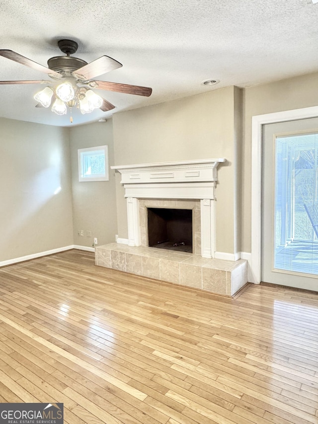 unfurnished living room featuring a textured ceiling, a fireplace, light wood-style flooring, and baseboards